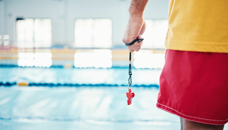 Nærbilde av badevakt i svømmehall som holder en fløyte i hånden.
