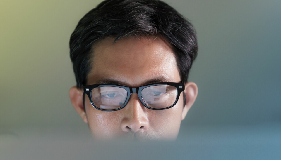 Nærbilde av en mann med briller som ser på en dataskjerm.