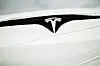 Nærbilde av Tesla-logoen på en ny bil pakket inn i plastfolie.