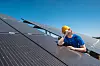 Montør står mellom solcellepaneler på et tak og ser mot sola.