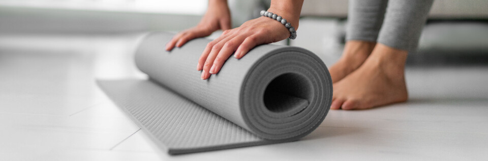 Forskning: Yoga hjelper mot jobbstress Nærbilde av barbeint kvinne som ruller ut en yogamatte.