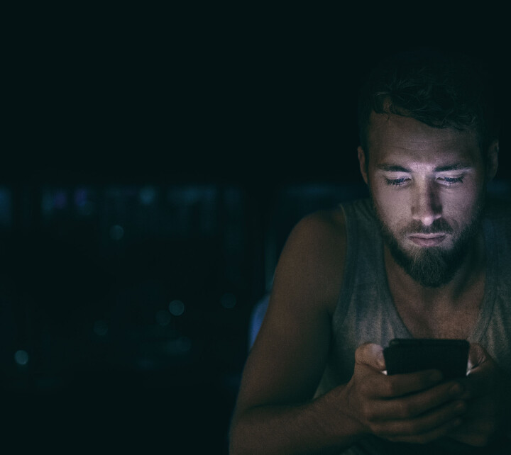 KRISE: En problemspiller herjes med av krefter han ikke har kontroll over. Ofte er det friske, unge menn som ikke har noen erfaring med å være i en livskrise. Ung mann sitter i mørket og spiller på telefonen.