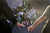 Bilde av lys og blomster på åstedet. To personer griper etter hverandres hender i forgrunnen.