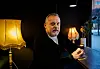 Mann sitter ved vindusbord på mørk kafé med to bordlamper i bakgrunnen