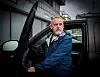 Mann i blå jakke går ut av en mørk bil foran et næringslokale