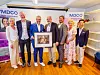 En gruppe mennesker poserer foran MDCO-bannere med en innrammet gave i sentrum.