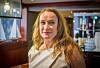 Smilende kvinne i lyst antrekk foran en bar med flasker og innredning.