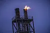 Flamme fra et fakkeltårn ved Equinors anlegg på Melkøya mot en mørk blå himmel.