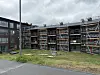 Fleretasjes bygning med stillaser, gressområde og vei under en overskyet himmel.