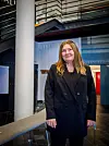 Kvinne i svart kåpe står i et moderne kontor- eller hotellinteriør.