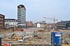 Stor byggeplass med kraner, bygårder og et høyt moderne tårn i bakgrunnen.