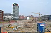 Stor byggeplass med kraner, bygårder og et høyt moderne tårn i bakgrunnen.