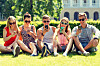 friendship, leisure, summer, technology and people concept - group of smiling friends with smartphones sitting on grass in park.