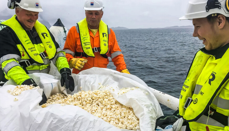 Tre oljearbeidere står med en stor pose popkorn. Havet i bakgrunnen.