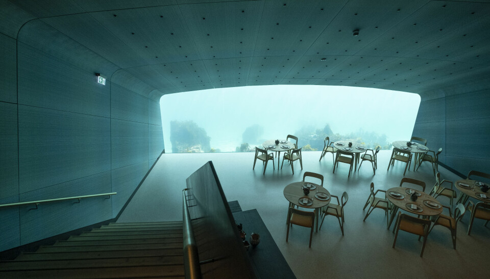 Interiørbilde fra restauranten. Flere restaurantbord, med vindu ut mot det det undersjøiske i bakgrunnen.