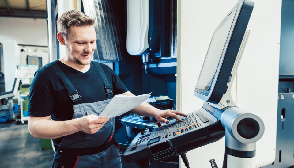 Mannlig industriarbeider/prosessoperatør betjener et kontrollpanel mens han studerer et dokument på papir.