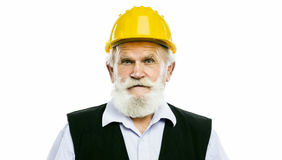 Portrett av eldre mann med skjegg og anleggshjelm.