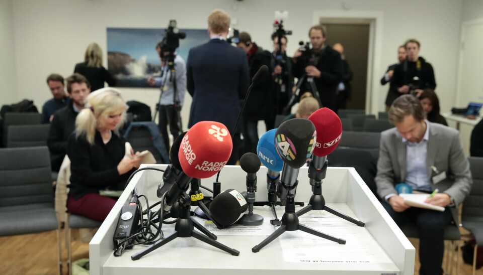 Mikrofoner fra en rekke mediehus på en talerstol. Journalister i salen bak.