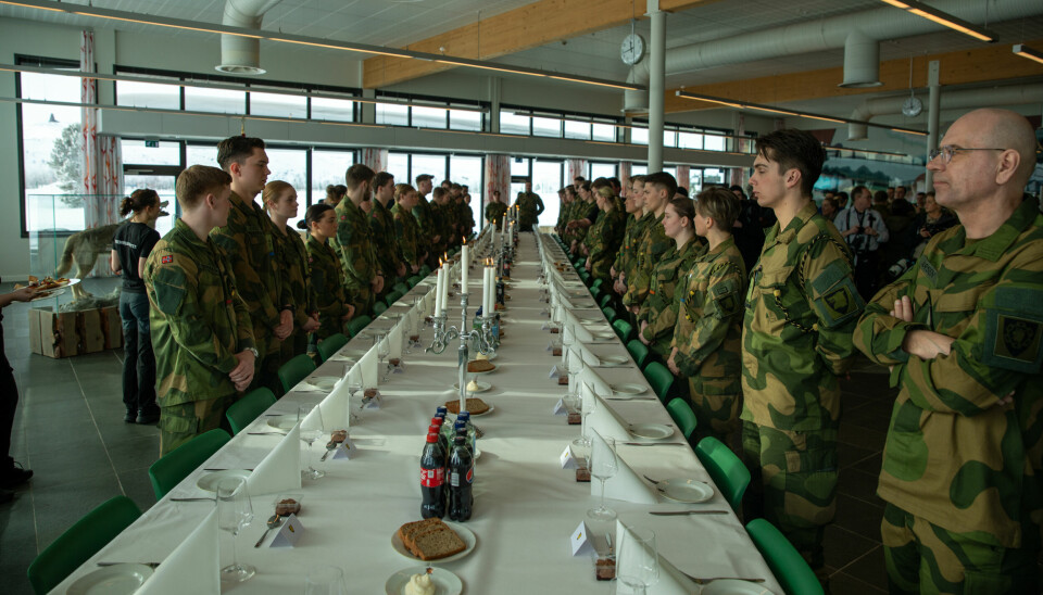 Bilde av uniformskledde offiserer og soldater som står og venter på å sette seg til bords. På bordet står brusflasker.