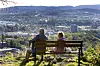 Et eldre par, en kvinne og en mann, sitter på en benk og ser ut over Trondheim.