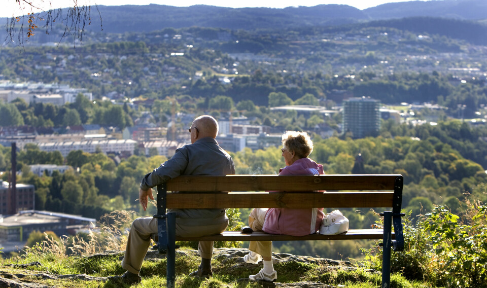 Et eldre par, en kvinne og en mann, sitter på en benk og ser ut over Trondheim.