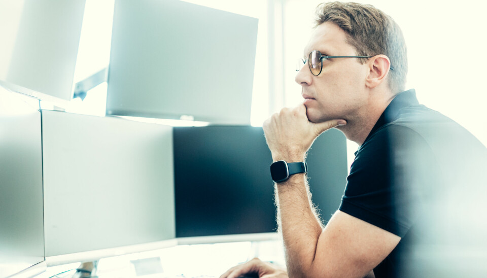 Mannlig kontormedarbeider studerer flere dataskjermer han har foran seg.