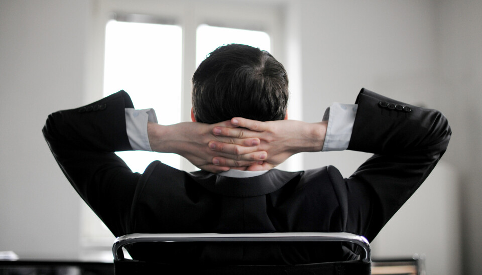 Mann med dress sitter tilbakelent på kontorstol med hendene foldet bak nakken.