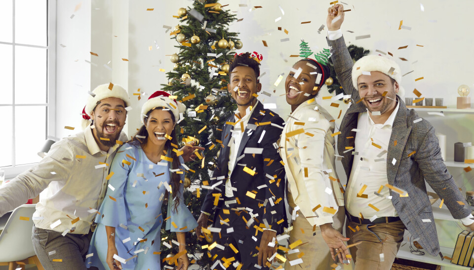 En gruppe smilende kolleger på kontoret, poserer med juletre, nisseluer og konfetti.