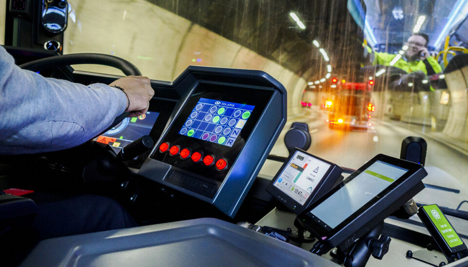 Nærbilde av hendene til en bussjåfør på rattet mens bussen kjører i en tunnel.