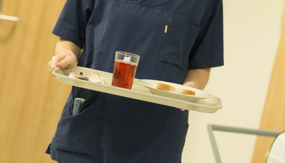 Kvinnelig pleier i uniform bærer et brett med mat til en pasient.